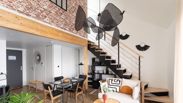 A modern living space with a dining area, a sofa, and a staircase with a black railing. - Le Saint Martin Bis - Bel appartement moderne et confortable (Rennes)