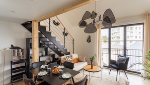 A modern living space with a dining area, staircase, and large windows offering a view of the city. - Le Saint Martin Bis - Bel appartement moderne et confortable (Rennes)