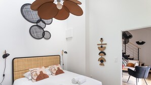 A modern bedroom with a large bed, a ceiling fan, and a view into the living area. - Le Saint Martin Bis - Bel appartement moderne et confortable (Rennes)
