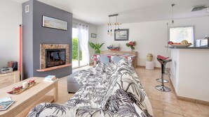 Una sala moderna con chimenea, un sofá grande, una mesa de comedor con sillas y una zona de cocina con taburetes de bar.