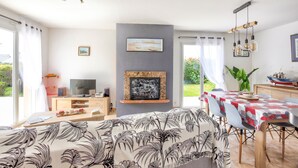 Una sala de estar moderna con chimenea, un comedor con mesa, y un televisor sobre un soporte de madera.