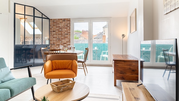 A modern living room with a dining area, a brick wall, and a large sliding glass door leading to a balcony. - L'Ingénieux - Appt près de la Place Zola (Nantes)