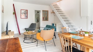 A modern living room with a wooden dining table, two sofas, a staircase, and a hanging light fixture. - L'Ingénieux - Appt près de la Place Zola (Nantes)