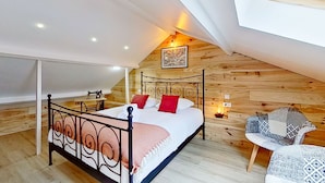 A bedroom with a sloped ceiling, a bed with a metal frame, a wooden wall, and a small table with a chair. - L'Ingénieux - Appt près de la Place Zola (Nantes)