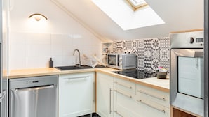 A modern kitchen with a dishwasher, microwave, oven, and patterned backsplash. - L'Ingénieux - Appt près de la Place Zola (Nantes)