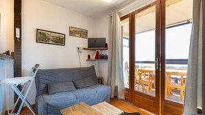 Ein Wohnzimmer mit grauem Sofa, Couchtisch aus Holz und Fernseher an einer Ablage.