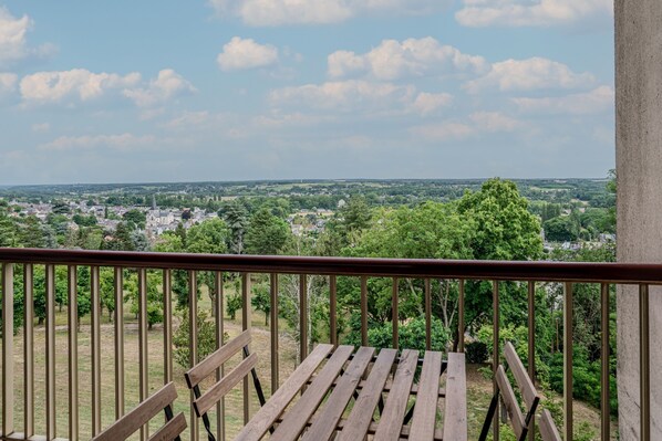 Ein Balkon mit einer hölzernen Bank mit Blick auf eine Stadtlandschaft mit Bäumen und Gebäuden.