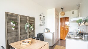 Eine kleine Küche mit einem Holzesstisch, Stühlen, einem Kühlschrank und einer hängenden Pflanze.