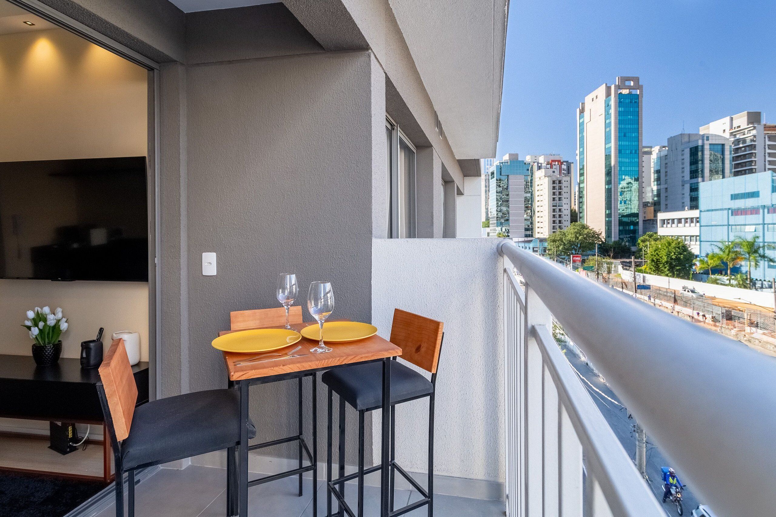 A balcony with a dining table set for two, a TV, and a potted plant.