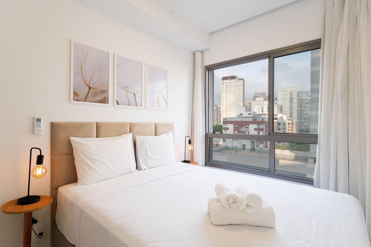 A hotel room with a large bed, a view of the city, and artwork on the wall.