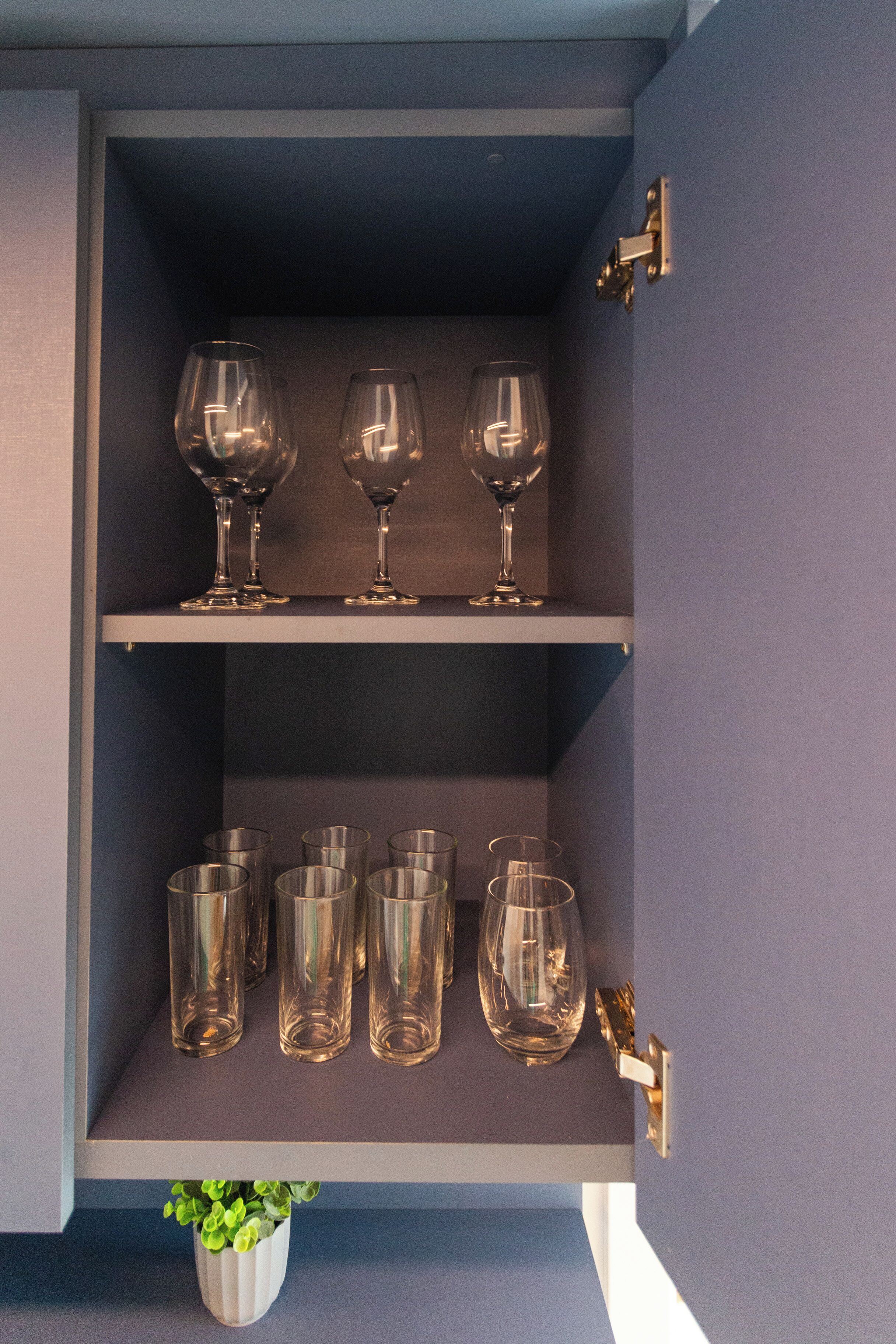 A cabinet with two shelves, one holding wine glasses and the other holding various glass tumblers.