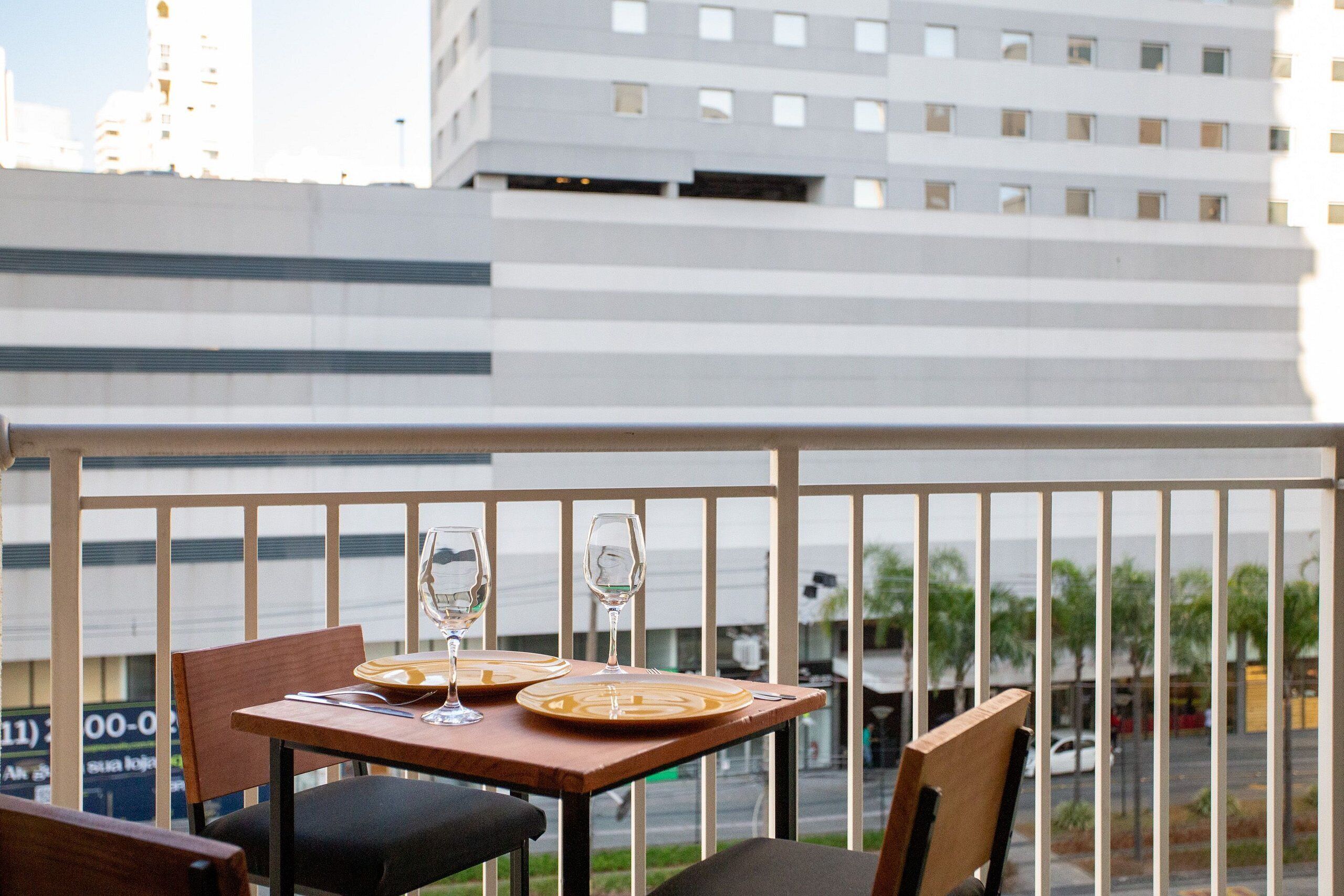 A balcony with a table set for two, overlooking a cityscape with modern buildings.