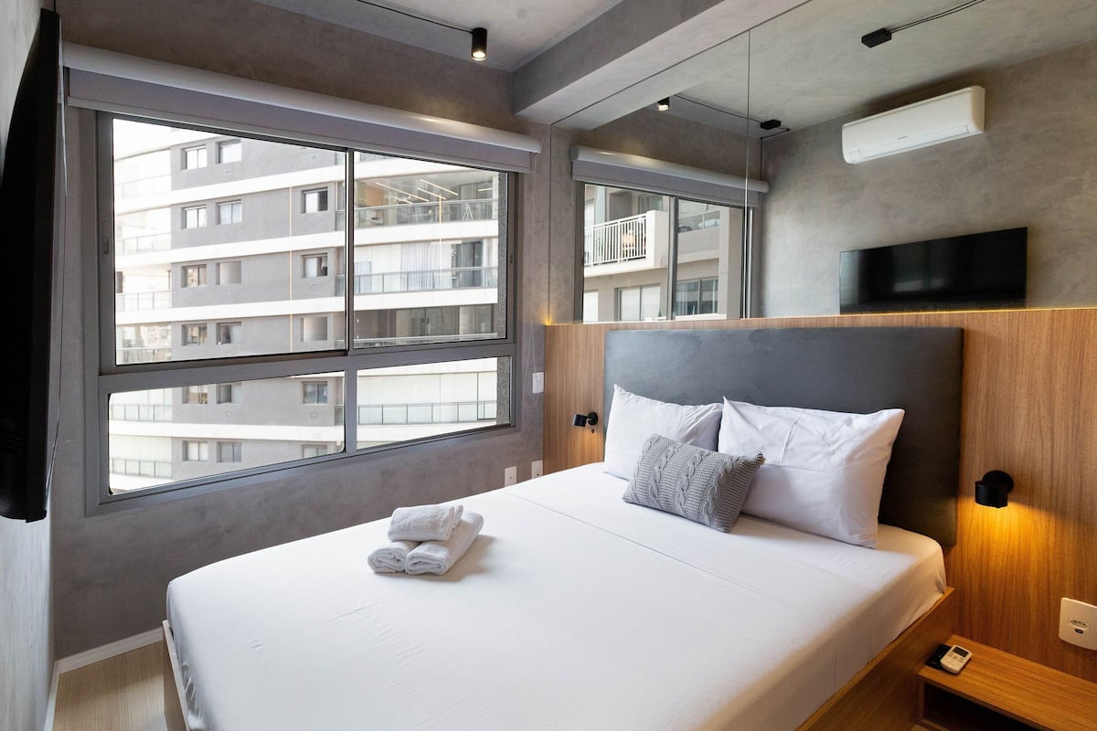 A modern hotel room with a large bed, a TV, and a window with a city view.