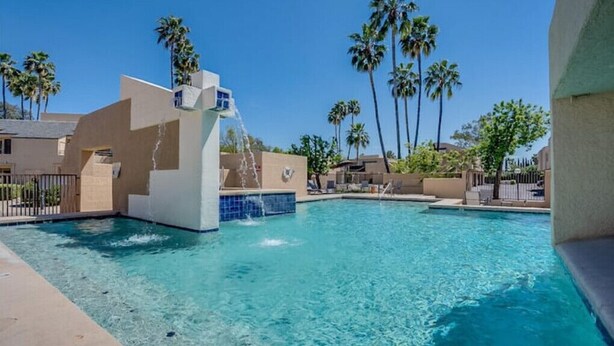 Una piscina con fontana, circondata da palme e edifici.
