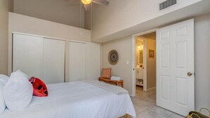 Una camera da letto con un letto, una ventola a soffitto, una porta e un corridoio che porta al bagno.