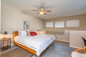 A bedroom with a bed, a ceiling fan, a bedside table, a lamp, and a window with blinds.