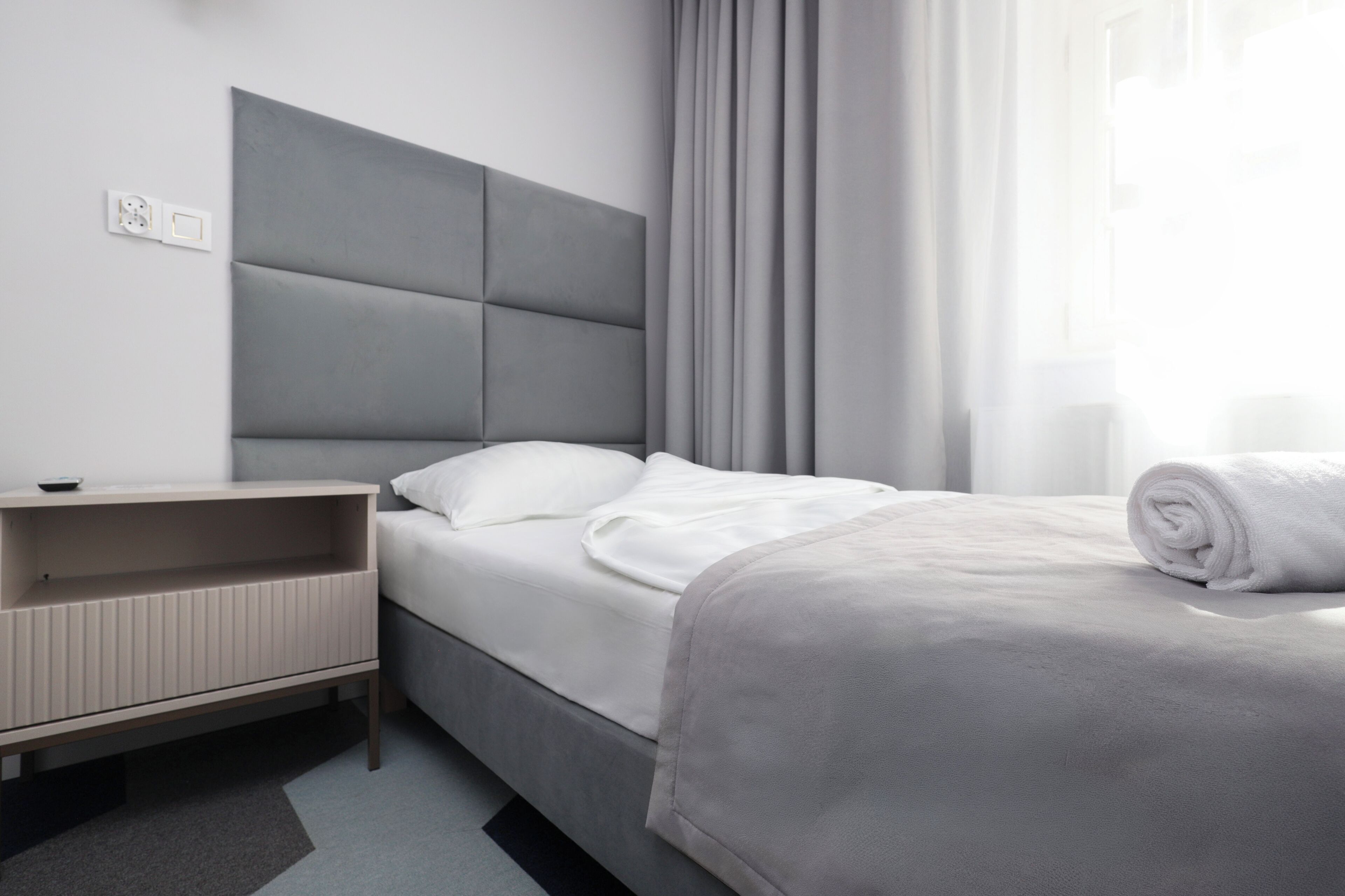Una habitación de hotel moderna con cama, mesita de noche y ventana con cortinas.