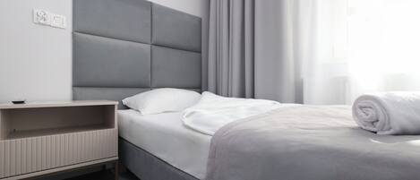 Una habitación de hotel moderna con cama, mesita de noche y ventana con cortinas.