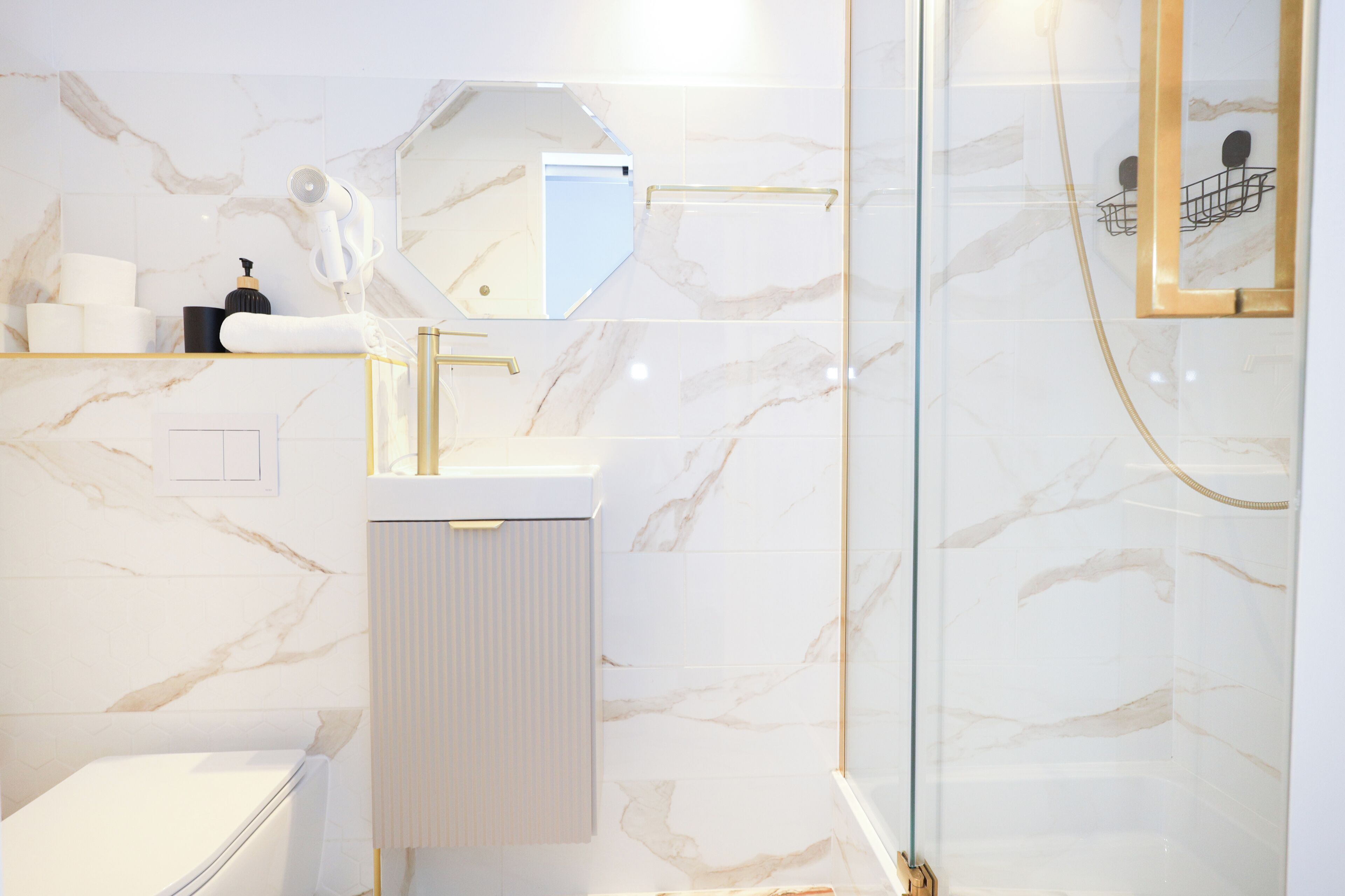 A modern bathroom with a glass shower enclosure, a white sink, and a marble-tiled wall.