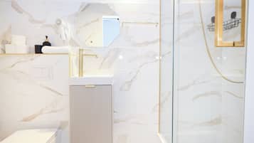 Un baño moderno con cabina de ducha de vidrio, un lavabo blanco y una pared revestida de mármol.