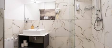 Un bagno moderno con doccia a vetro, un lavandino bianco con mobile nero e una parete rivestita in marmo.