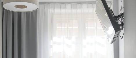 Une chambre à coucher avec un lit, un pouf vert, une lampe fixée au mur et une fenêtre avec des rideaux.