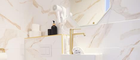 A modern bathroom with a white toilet, a gold faucet, and a marble backsplash.