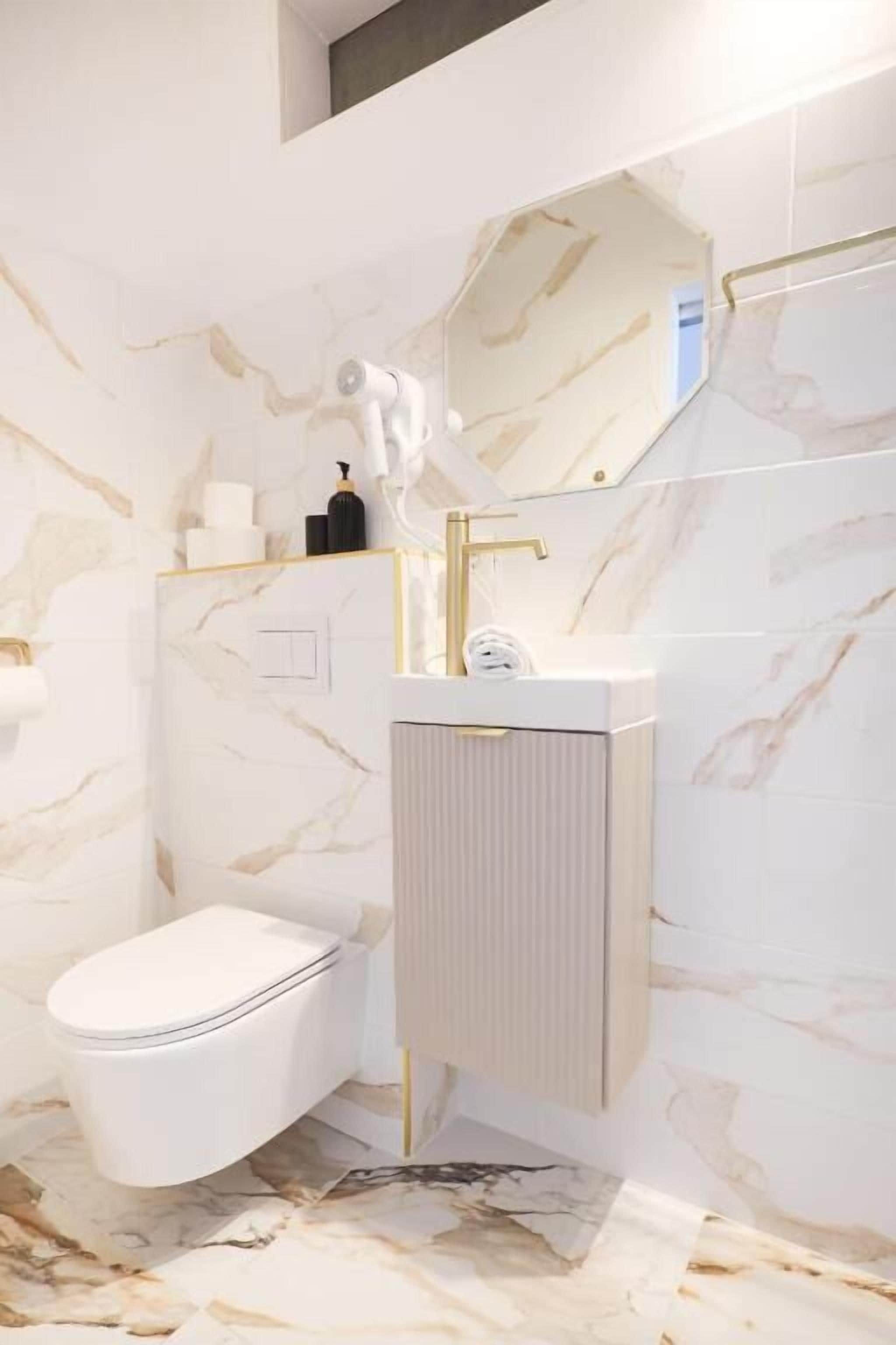Een badkamer met een wit toilet, een gouden kraan en een wand met een marmerprint.