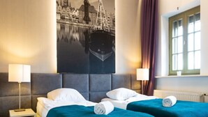 A hotel room with two beds, a cityscape painting, a window with curtains, and a wooden floor. - Moon Apartments Gdańsk (Gdansk)