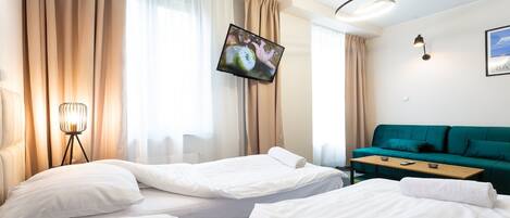 A hotel room with two beds, a green sofa, a TV, and a lamp.