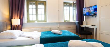 A hotel room with two beds, a desk, a TV, and a window with curtains.