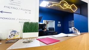 A reception desk with a neon sign, a computer, and a plant. Signs indicate room numbers and directions. - Moon Apartments Gdańsk (Gdansk)