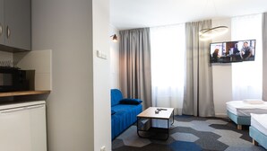 A hotel room with a kitchenette, a blue sofa, a small table, a bed, and a TV. - Moon Apartments Gdańsk (Gdansk)