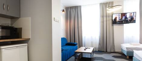 A hotel room with a kitchenette, a blue sofa, a small table, a bed, and a TV.