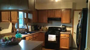 A kitchen with wooden cabinets, a black stove, a sink, and a countertop with a fruit bowl. - 3 Bedroom, 2 Bathroom Home - EAA Rental Only (Oshkosh)