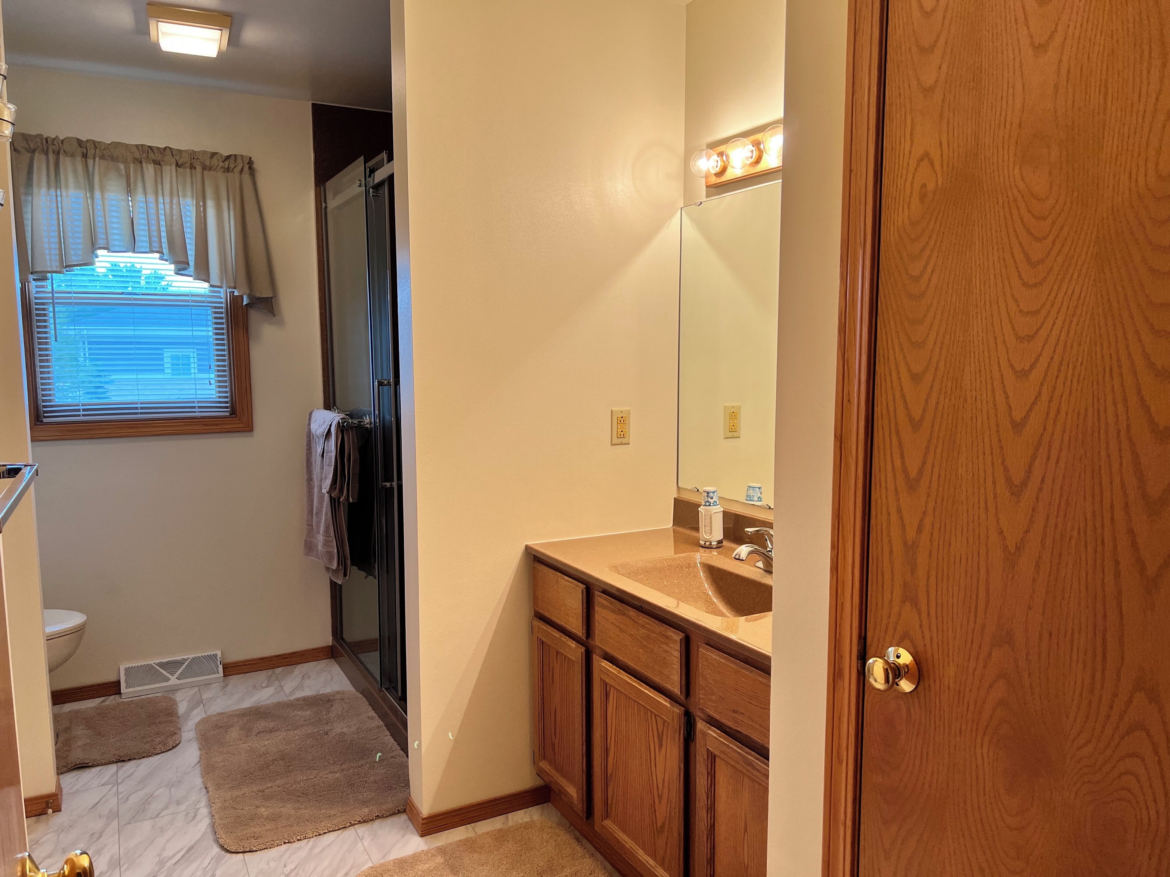 A bathroom with a wooden vanity, a mirror with lights, a toilet, and a shower area.