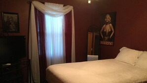 A hotel room with a large bed, a television, a poster of Marilyn Monroe, and a window with curtains. - 3 Bedroom, 2 Bathroom Home - EAA Rental Only (Oshkosh)