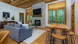 A modern living room with a stone fireplace, a large TV, and a wooden ceiling. - NEW Modern Cabin! 
2 King suites, hot tub, fire-pit and 2 fireplaces! (McCaysville)