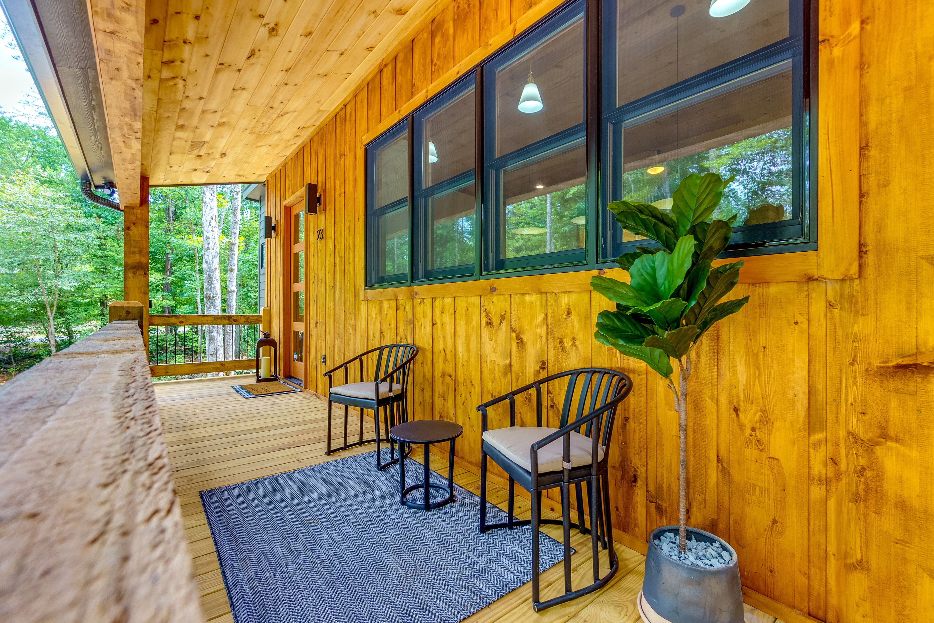 Eine Holzterrasse mit zwei Stühlen, einem Tisch, einem Topfpflanzen und Blick auf den Wald.