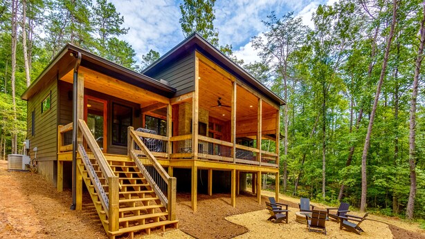A two-story cabin with a covered porch, outdoor seating area, and a staircase leading to the upper level. - NEW Modern Cabin! 
2 King suites, hot tub, fire-pit and 2 fireplaces! (McCaysville)