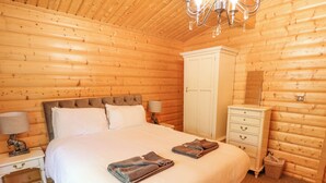 Une chambre aux murs lambrissés, avec un grand lit, une armoire, une table de chevet et une lampe.