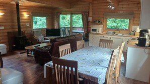 Un chalet confortable comprenant une table à manger, des chaises, un canapé, un téléviseur, un poêle et un coin cuisine équipé d’un four à micro-ondes et d’un évier.