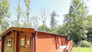 Une cabane en bois dotée d’un porche et d’une petite terrasse, entourée d’arbres.