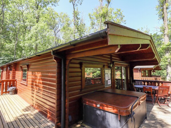 A wooden cabin with a deck, a hot tub, and a dining area with outdoor furniture. - 64 Acorn Lodge Kenwick Park (Louth)