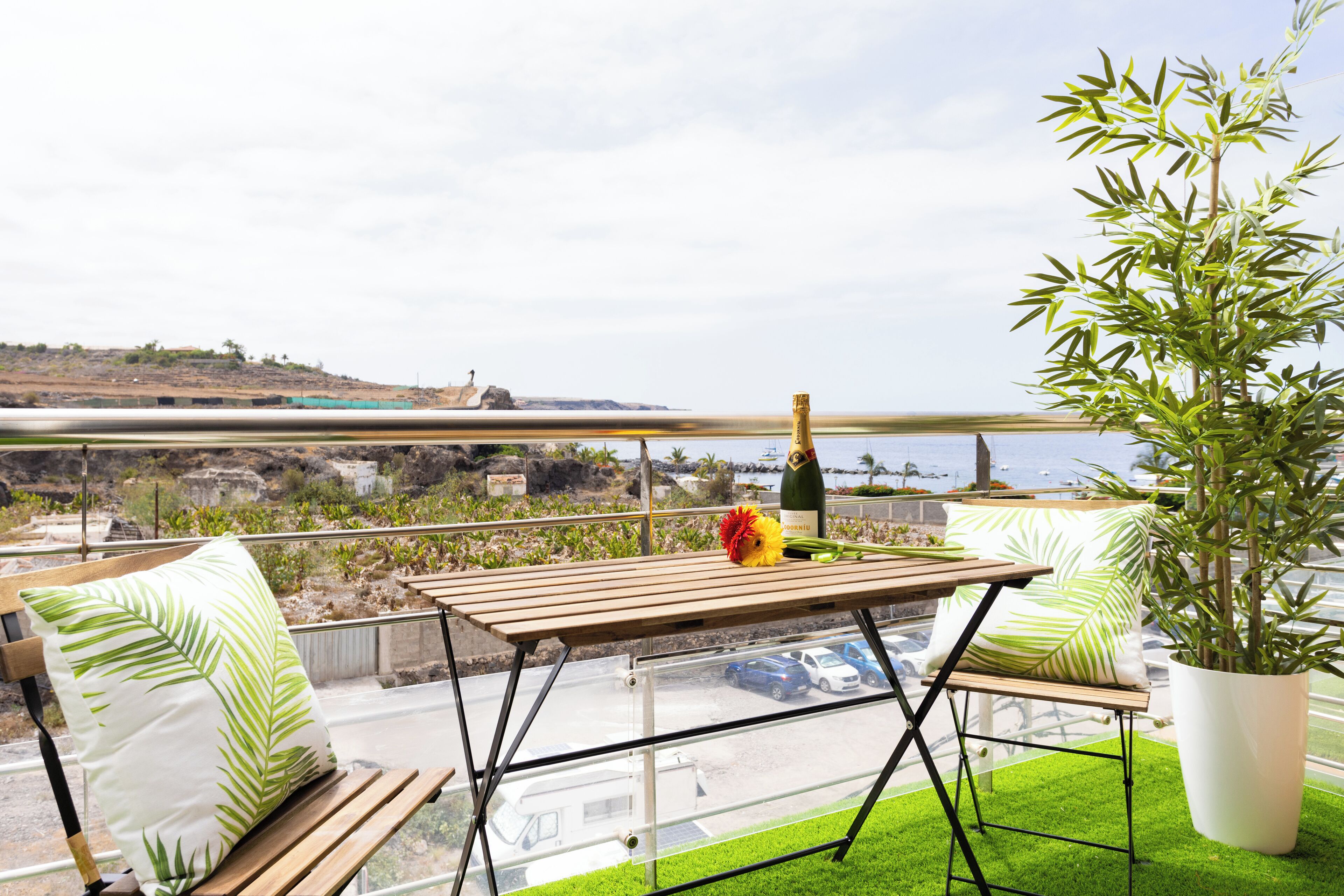 A balcony with a wooden table, two chairs, a potted plant, and a bottle of champagne.