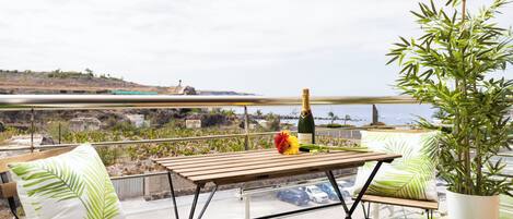 A balcony with a wooden table, two chairs, a potted plant, and a bottle of champagne.