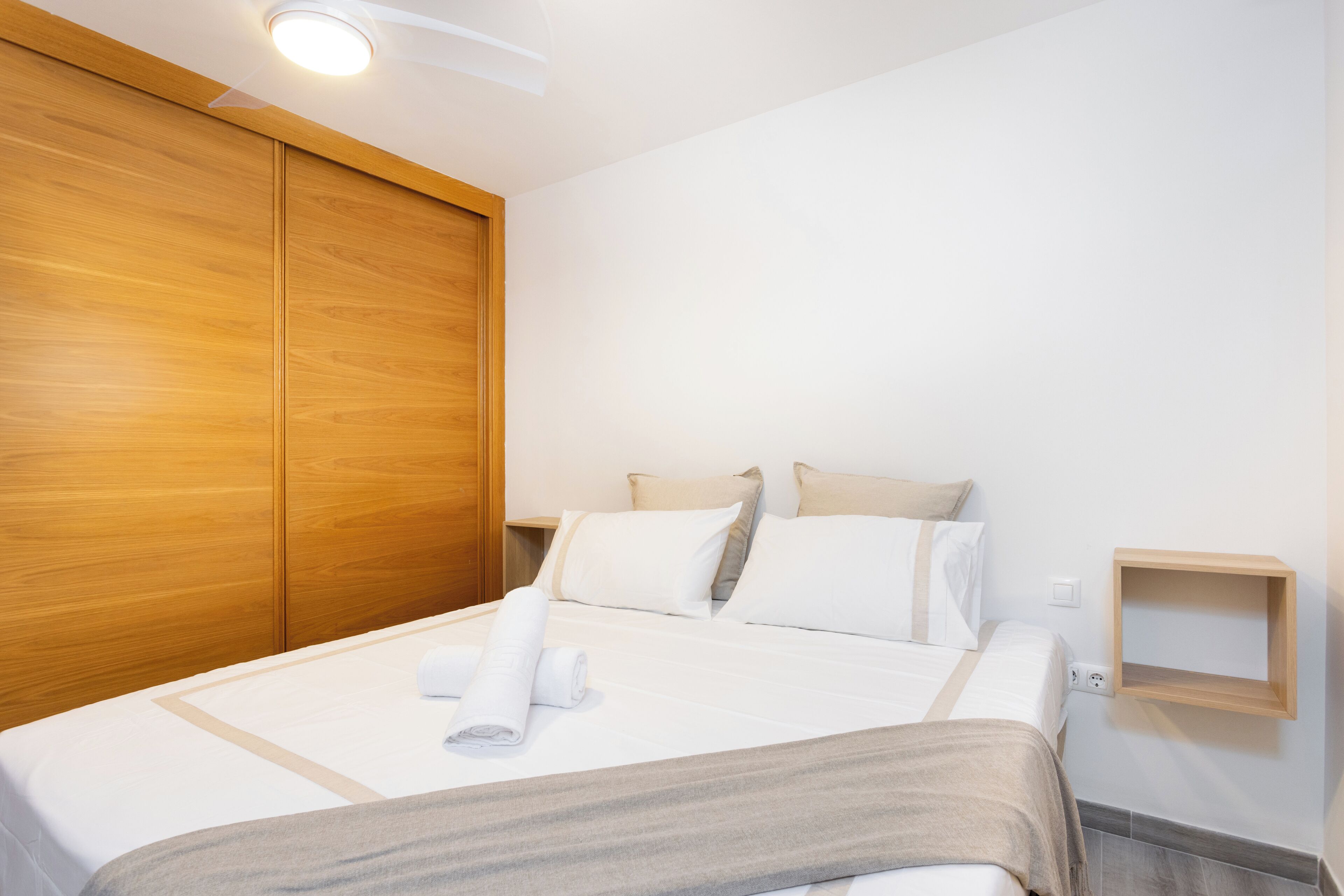 A hotel room with a large bed, wooden wardrobe, and a small wooden shelf.