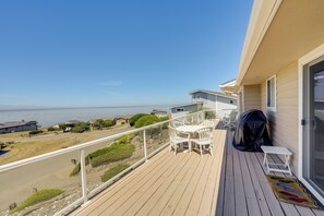 Ein Balkon mit Blick auf den Ozean, weiße Gartenmöbel und eine überdachte Grillgelegenheit.