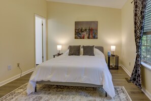 Une chambre à coucher avec un lit, deux tables de chevet, un tableau au mur et une fenêtre avec des rideaux.