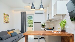 A modern kitchen with a wooden table, two white chairs, a grey sofa, and a grey curtain.